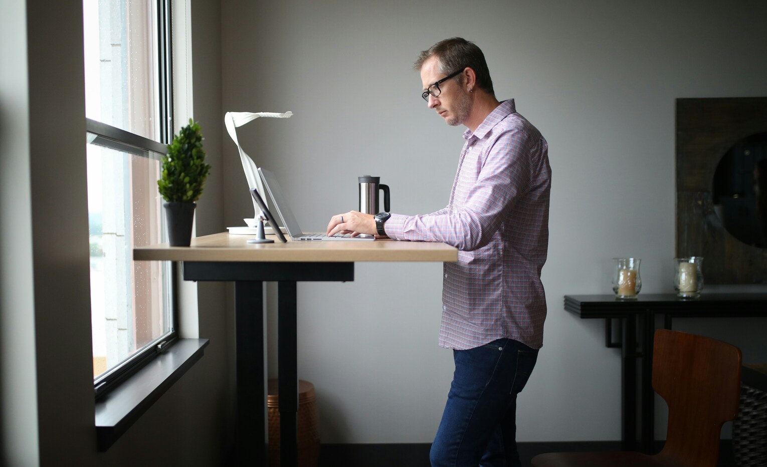 Man typing at a height-adjustable standing desk near a window
