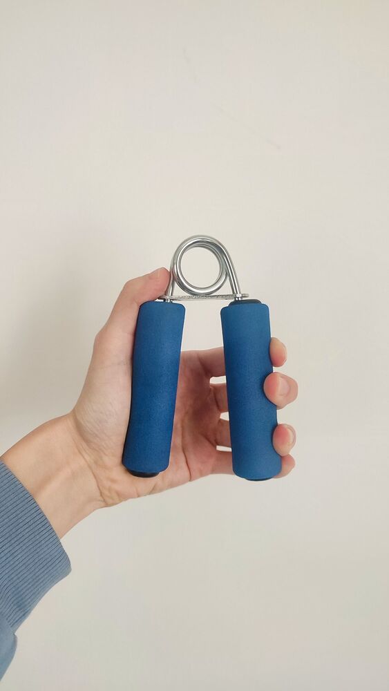 Hand holding a blue spring hand gripper against a light wall