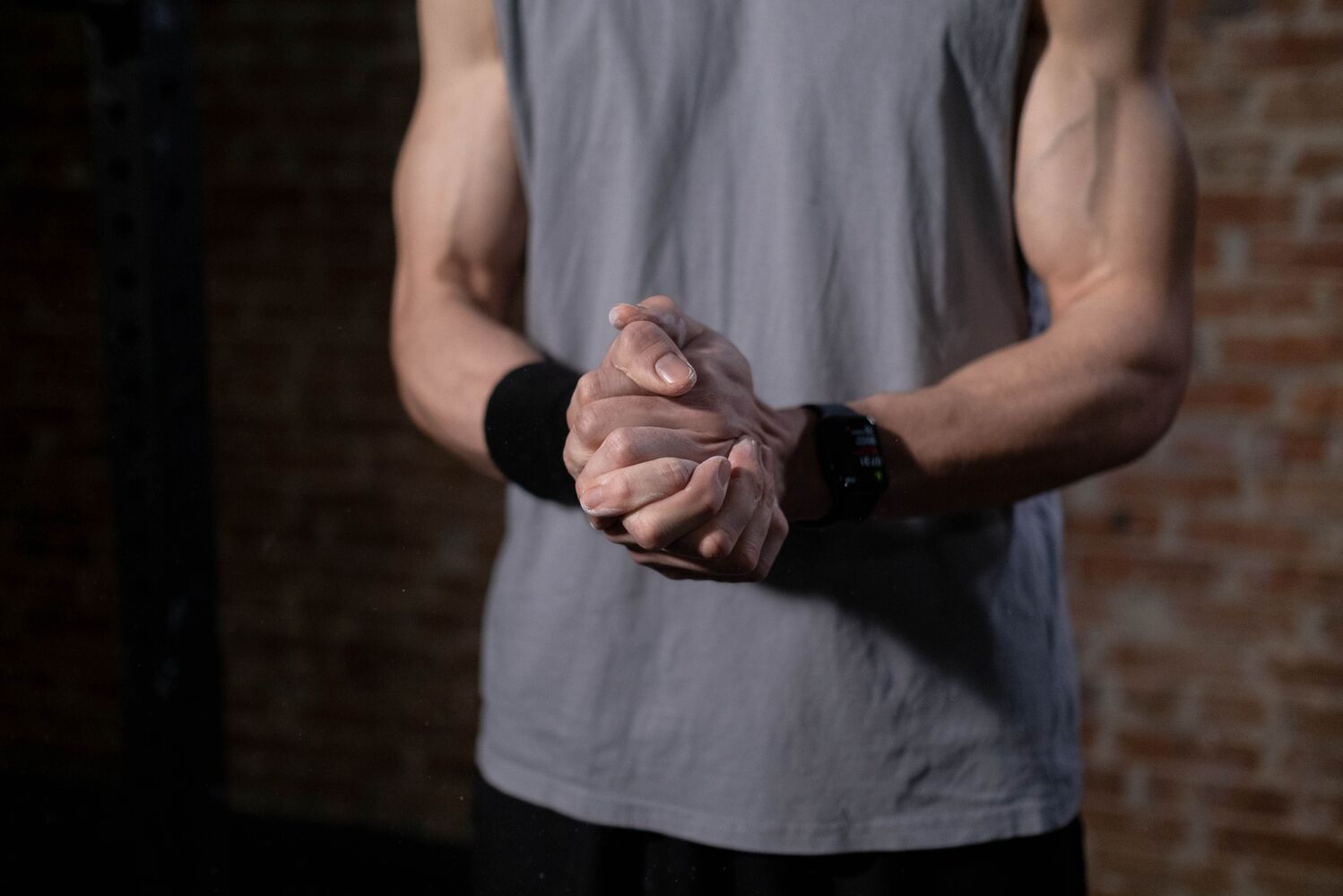 Person in a grey sleeveless shirt gently clasping both hands in front of a brick wall